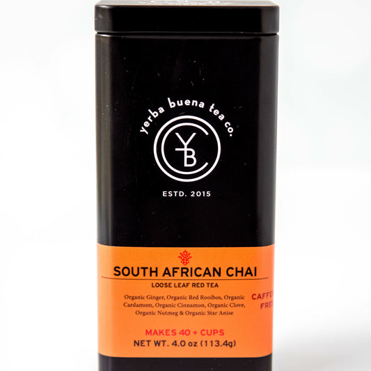 A black tin of Yerba Buena Tea Co.'s South African Chai loose leaf rooibos tea, labeled as caffeine-free and made with organic red rooibos, ginger, cinnamon, cardamom, cloves, and nutmeg, on a white background.