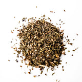 Loose leaf herbal tea blend scattered in a pile with dried leaves and botanicals on white background, by Yerba Buena Tea Company.