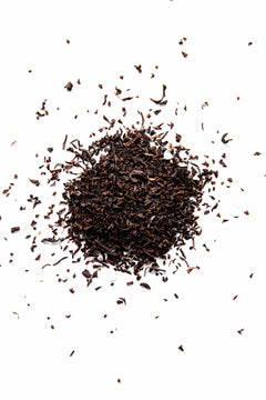 A close-up top-down view of Yerba Buena Tea Co. Irish Breakfast loose leaf black tea, showing a pile of dark, finely cut organic black tea leaves on a white surface.