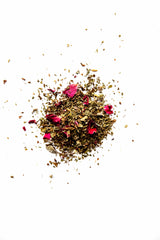 A close-up view of Yerba Buena Tea Co. Prana Balance loose leaf herbal tea, displaying a colourful organic blend of green herbs and vibrant pink rose petals on a white surface.